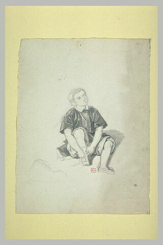 Jeune garçon, assis par terre, rattachant sa sandale droite, image 1/1